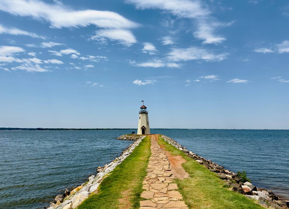 The grass-lined path to the Lake Hefner Lighthouse, surrounded by water.