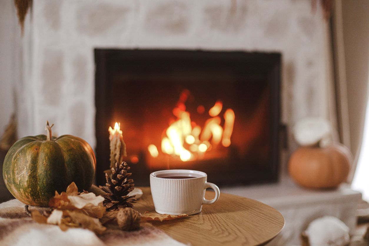 A cozy fall-themed coffee table with a pinecone, coffee, a painted pumpkin, and a burning fireplace