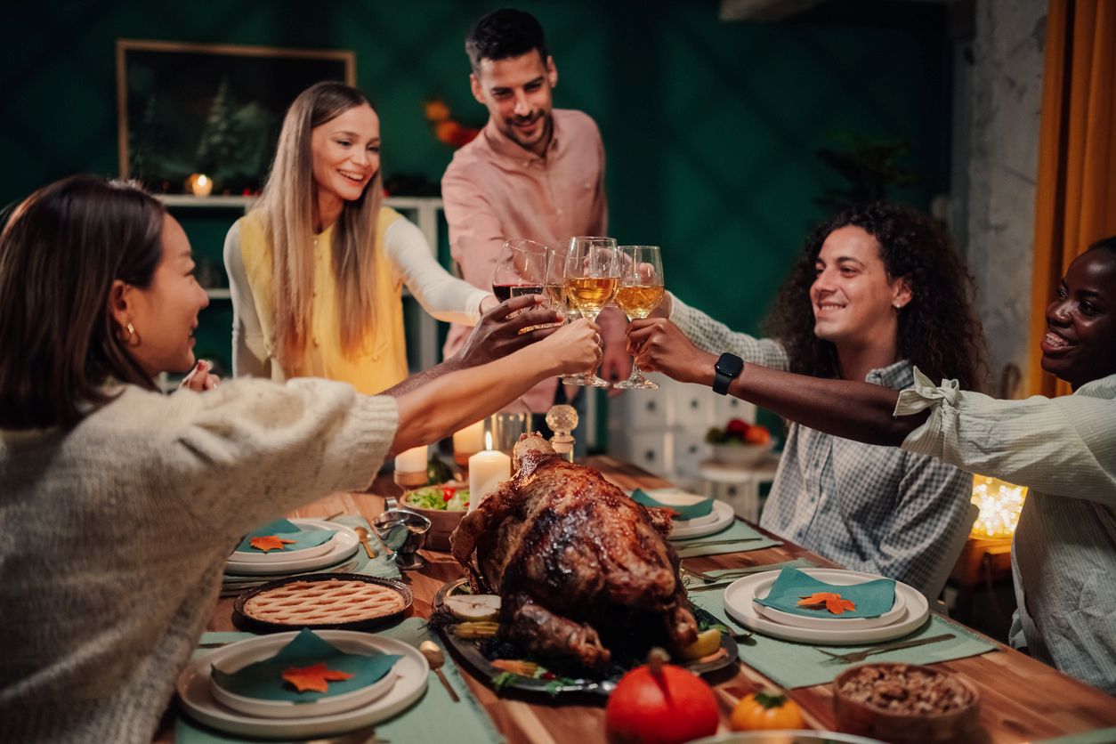 A group of adult friends celebrate Friendsgiving while toasting their wine glasses.