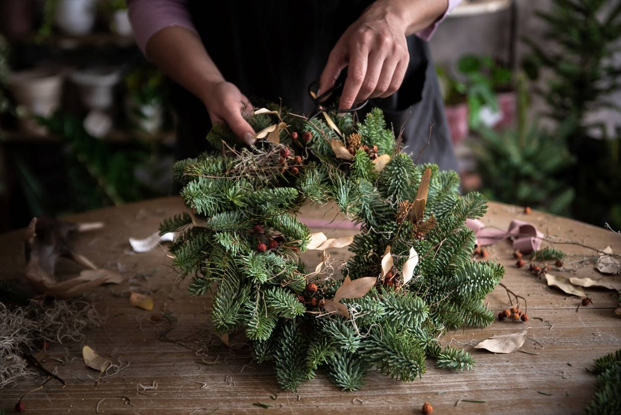 A woman carefully cuts evergreen branches to make a homemade Christmas wreath.