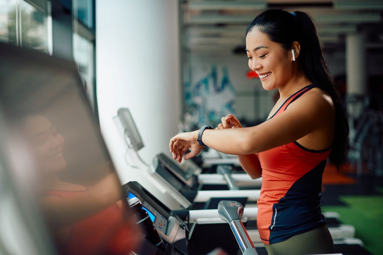 A woman checks her vitals as well as the time on her watch while working out on a treadmill.