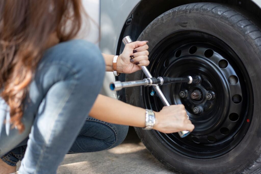 A woman tightens the lug nuts on her wheel after attaching a spare tire to her car.